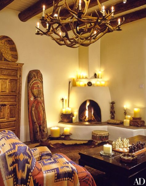 In the living room, a carved and painted totem from New Guinea rests beside the kiva-style fireplace. Atop the armoire is a Papago cradle basket. The Mexican church candles throughout were made especially for Kent’s shop. Western Home Decor Living Room, Santa Fe Interior Design, Santa Fe Style Decor, Southwest Interior Design, Santa Fe Interiors, Southwest Interior, Western Interior Design, Santa Fe Decor, Santa Fe Style Homes