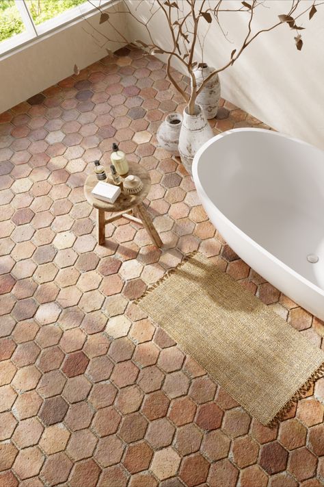 Top view of primary bath design with terracotta hexagon floor tile, white bathtub in center of room, wooden bathroom stool. Terracotta Flooring Bathroom, Terracotta Tile Shower Floor, Terra Cotta Tiles Bathroom, Terracota Floor Bathroom, Terra Cotta Floors Kitchen, Terra Cotta Floor Bathroom, Terra Cotta Shower Tile, Brick Floor In Bathroom, Terra Cotta Floors Bathroom