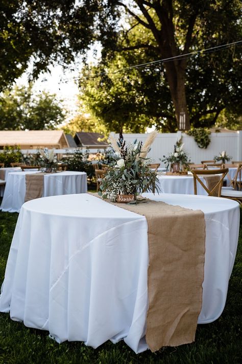 White tablecloths are decorated with beige table runners and floral arrangements in a Chico, CA backyard wedding White Tablecloth With Burlap Runner, Beige And White Decor Party, Wedding Table Covers Ideas Tablecloths, Round Party Tables, Reception Table Cloth Ideas, White Table Clothes Wedding, White And Wood Party Decor, White Table Cloth With Burlap Runner, White And Beige Table Decor