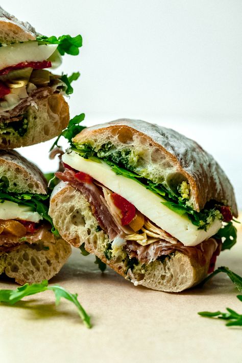 Antipasto Sandwich with Lemon-Basil Pesto | All of your favorite flavors from an antipasto board, all wrapped up in sandwich form!  Layers of lemony basil pesto, salami, prosciutto, mozzarella and provolone cheeses, arugula, artichokes and hot and sweet roasted peppers make this burst with flavor.  Make in advance and let the flavors get to know each other in the fridge-then eat this cold, at room temperature or hot as a pressed sandwich!   #food #recipe #antipasto #lunchideas #sandwichrecipes Shower Sandwiches, Antipasto Board, Hiking Lunch, Lemon Basil Pesto, Prosciutto Mozzarella, Lunch Sandwiches, Captain Crunch, Pressed Sandwich, Not Hungry