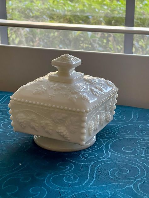 This is a vintage Westmoreland Milk Glass Square Candy Dish, approximately 4-1/2" in diameter, with a circular pedestal.  It has a grapevine theme and small beaded edges.  Love the beaded edges.  It is in excellent vintage condition with no chips or cracks.  The symbol is inside the center of the lid and is the intertwined W and G.  It is very hard to see; in fact, I had to use a magnifying glass.  I tried to get a good photo of it, but it was nearly impossible.  See the last photo. What is the symbol for Westmoreland Glass? The first mark was a "W" found inside of a Keystone which can be found from the period of 1910 through the mid 1940s. The second mark, which is the more commonly known by collectors and dealers, is the intertwined W and G that Westmoreland began to use in 1946 on most Westmoreland Glass, Good Photo, White Milk Glass, Magnifying Glass, Candy Dish, Candy Dishes, Milk Glass, Glass Collection, Grape Vines