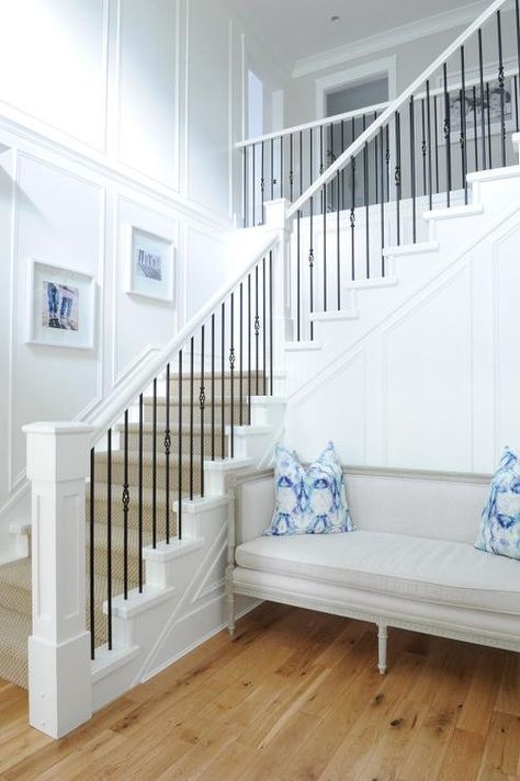 Chic foyer features a white staircase accented with iron spindles lined with a sisal rug. A wainscoted staircase wall is lined with a gray French settee accented with blue pillows. Stairs Metal, Stair Railing Makeover, Iron Stairs, Metal Spindles, White Staircase, White Stairs, Iron Staircase, Diy Staircase, Iron Stair Railing