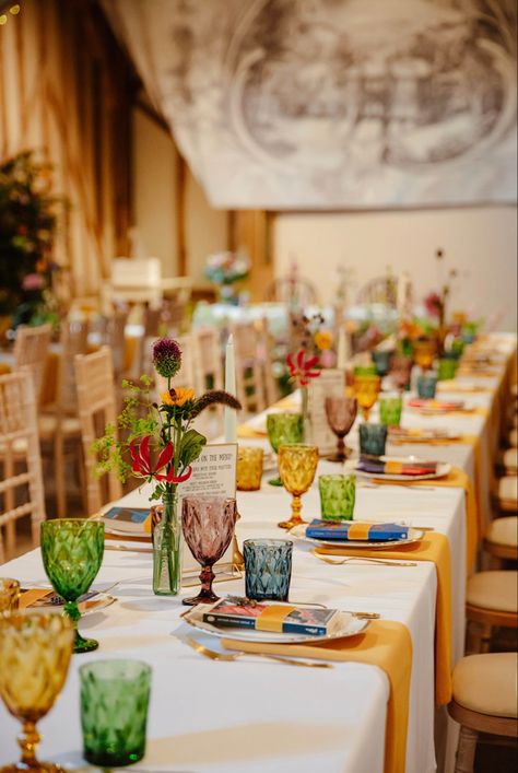 Tablescape using multi-coloured goblets and tumblers, gold napkins and whimsical floral displays in mismatched vases. #Wedding #Tablescape #Colorful #Gold #Barn #Summer #Design #WeddingStyle 📸 Zara Davis Wedding Reception Colored Goblets, Mismatch Decor, Mismatched Table Setting Mix Match, Eclectic Wedding Place Settings, Coloured Glassware Wedding, Colored Glass Table Setting, Wedding Colored Glassware, Mismatched Vases Wedding, Multicolored Glassware Wedding