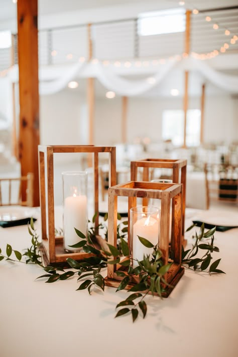 Rustic wooden rectangular candle holders for a fall centerpiece for the guest tables. Tables accent with white china plates, dark green satin napkins, and sprigs of greenery at this real indoor fall wedding reception at Emerson Fields in Missouri. Centerpiece Rustic Wedding, Wedding Centerpiece Rustic Elegant, Simple Greenery Table Centerpieces, Wedding Centre Pieces Without Flowers, Rustic Centerpiece Wedding Diy, Rustic Wedding Decor Eucalyptus, Wooden Candle Holder Centerpiece, Wedding Guest Table Decorations, Deep Green Wedding Table Decor