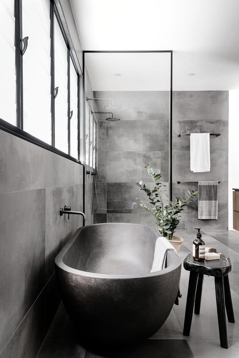 A modern master bathroom with large format grey tiles, a grey freestanding bathtub, and a black framed glass shower screen. Bathroom Black Bathtub, Industrial Bathroom With Bathtub, Grey Bathtub Ideas, Grey Industrial Bathroom, Black Bathtub Bathroom Ideas, Black Bathtub Bathroom, Bathtub Concrete, Open Bathtub, Grey Bathtub