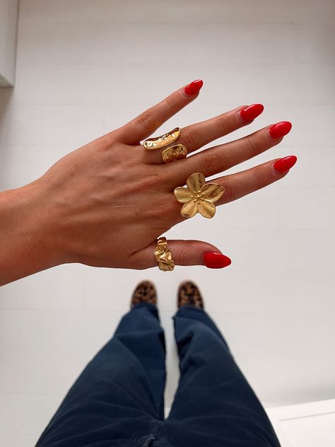 A close-up of a hand with red nail polish, wearing multiple gold rings including a flower ring, against a background of pants and leopard print shoes Summer Jewelry Stack, Chunky Ring Stack, Maximalist Jewelry, Chunky Gold Jewelry, Photography Styling, Chunky Jewelry, Jewelry Essentials, Jewelry Lookbook, Stacked Jewelry