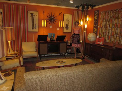 I love everything about this room except the musical artwork and the orange walls. It makes it too dark! And the manequin can find a new home...-CAB Mid Century living room display Mid Century Movie Room, 1960s Lounge Room, Dark Mid Century Modern Living Room, 70s Inspired Music Room, Red Mid Century Modern Living Room, 70s Orange Living Room, Orange Retro Couch, 1970s Living Room, Retro Homes