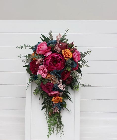 Featuring a striking mix of fuchsia, teal, burgundy, and gold blooms, complemented by lush greenery, this design is perfect for making a statement. Whether you're going for a modern chic or a romantic boho look, this bouquet will capture the eye and heart of every guest. #CascadingBouquet #cascadingflowers #fallwedding #fauxflowerarrangement #fauxweddingflowers #artificialbouquet #tealbouquet #pinkbouquet #WeddingBouquets #bridalbouquet #weddingflorist Wedding Emerald Green, Jewel Tone Wedding Flowers, Teal Bouquet, Teal Burgundy, Faux Bouquet, Cascading Flowers, Jewel Tone Wedding, Artificial Bouquet, Faux Flower Arrangements