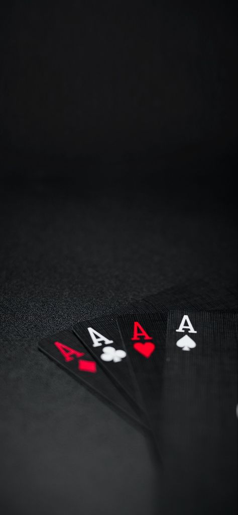 A wallpaper for your device.  Mostly black, very dark, with four cards spread in a fan on a black table or surface.  The order of the cards from left to right: ace of diamonds, ace of clubs, ace of hearts, and ace of spades.  The cards are black with the ace of hearts and ace of diamonds with read font and read symbols, and the ace of clubs and ace of spades with white colored font and symbols. Black Cards Wallpaper, Ace Of Spades Wallpaper Iphone, Wallpaper Cards Poker, Ace Card Wallpaper Iphone, Poker Card Wallpaper, Ace Of Spades Wallpaper, Poker Wallpapers, Black Poker Cards Wallpaper, Hd Phone Backgrounds