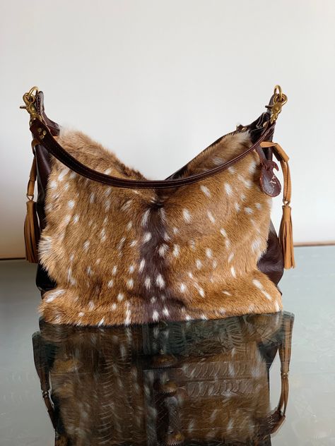 "Axis deer skin is supple and lustrous.This practical bag is a medium size, 14\"wide, 15\" long and an adjustable gusset maximum 4\". The front showcases the spotted design of the fur on Axis deer skin and the back and base are top grain light brown genuine leather. Fully lined with 3 pockets. There is a pocket in the back with a brass snap button. The sides have leather tassel and a toggle to cinch the sides. The base has brass feet. The handle is a repurposed leather belt with a braided design Axis Deer, Babies Pics, Mood Bored, Deer Hide, Western Purses, Practical Bag, Deer Skin, Pretty Bags, Leather Tassel