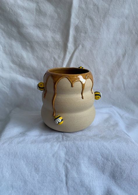 A unique, one of a kind pot handmade by me! This bumblebee pot is the perfect size for a small houseplant. The cute bees would be happy to look after whatever you choose to plant inside! How it's made: The shape is hand thrown on a pottery wheel, and the ceramic bees are hand crafted and painted before being attached to the main shape. I then use a golden yellow glaze and allow it to drip down the piece to mimic honey coming out of the bumblebee home. The piece is finally fired in a pottery kiln Ceramic Bees Pottery, Cute Ceramic Plant Pots, Cute Pottery Vase, Creative Pinch Pot Ideas, Honey Pot Pottery, Animal Vessels Ceramics, Flower Pottery Ideas, Small Vase Pottery, Plant Pot Pottery Ideas