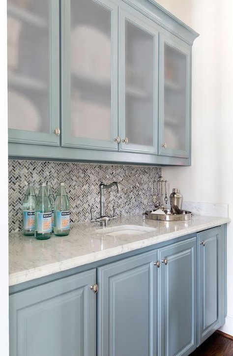 Blue bar features frosted glass upper cabinets and blue lower cabinets paired with white marble countertops fitted with a curved sink and vintage faucet as well as blue and gray marble chevron backsplash. Glass Upper Cabinets, Light Blue Paint Colors, Choosing Paint Colours, Painted Kitchen Cabinets Colors, Frosted Glass Door, Trending Paint Colors, Cabinet Paint Colors, House Of Turquoise, Kitchen Paint Colors