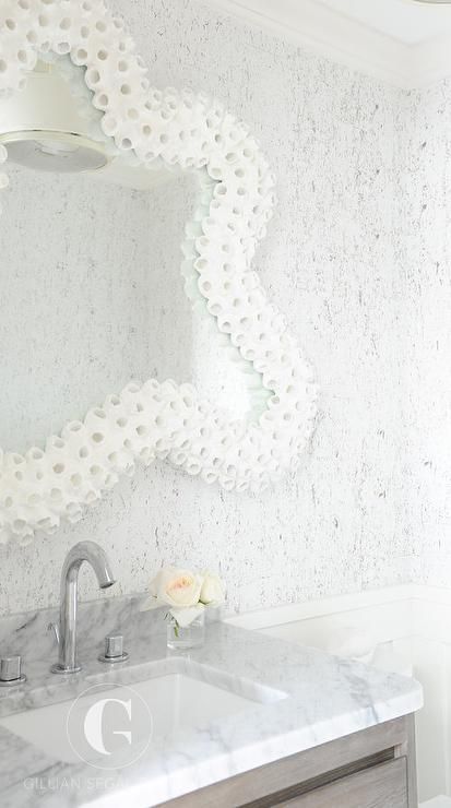 Gorgeous white and gray beach bathroom boasts a gray wash washstand topped with a carrera marble countertop fitted with an undermount sink and polished nickel gooseneck faucet mounted in front of a carrera marble backsplash fixed beneath a white coral framed mirror mounted to a white and gray wallpapered wall. Carrera Marble Backsplash, Half Bath Wallpaper, Octopus Bathroom, Coral Mirror, Beachy Bathroom, Beach Bathroom, Dream Beach Houses, Carrera Marble, Coastal Bathrooms