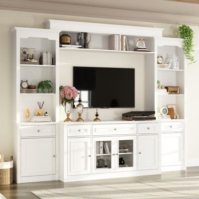 This wall unit features a 57-inch console, two pier units, and an overhead bridge providing ample storage options. This media unit features sliver finished knobs, glass doors with wood framing, open storage, and storage drawers. The console will accommodate most 55" TV. The elegant and minimalist white finish is suitable for any home decoration environment. | Wildon Home® Inverleigh Entertainment Center for TVs up to 55" Wood in Brown / White | Wayfair Modern Tv Stand Wall, White Tv Cabinet, Built In Wall Units, Entertainment Wall Units, Built In Shelves Living Room, Living Room Wall Units, White Tv Stands, Living Room Entertainment Center, Entertainment Wall