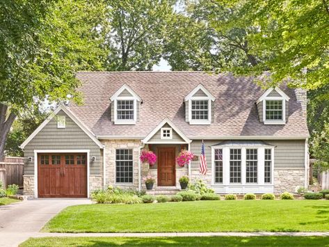 Location: Minneapolis Built in: 1940 Size: 3,900 sq. ft. Paint colors: (house) Sutton Place Grey and (trim) Crisp Linen White, Glidden “When we bought the home, it had steel siding and a flat front. We changed the steel to stone veneer, added siding that mimics the look of cedar shakes and put on a charming portico," say homeowners Amy and Mike Kolar. Dormer windows, like the ones here, are a classic detail of Cape Cod–style homes. They help carve more interior space under the steeply pitched ro Light Gray Cape Cod House Exterior, Cape Cod Siding Ideas, 1950s Cape Cod House, Cape Cod Style House Exterior, Home With Dormers, Exterior Vinyl Siding Colors, Homes With Curb Appeal, Cape House Exterior, Cape Cod Style Homes