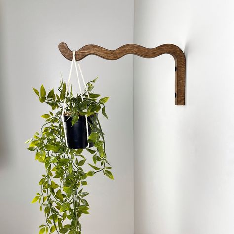 "Welcome your foliage into your decor with the long wavy wall plant hook! This 12\" wooden bracket makes for a stylish addition to your walls; the long length gives room for any hanging plants while its artistic wave adds an elegant touch. Installing is a breeze; all the hardware for secure mounting on concrete or brick walls is included. DIMENSIONS: Plant Hanger Hook (LxH) - 12\" (30 cm) x 6\" (15 cm) PRODUCT MATERIAL: Birch Plywood, hand-finished COLOR: Walnut MAX LOAD: Up to 11 lb (5 kg) DETAILS: Includes mounting hardware:  - (2x) 60mm Phillips Head Screws   - (2x) Plastic Brick/Concrete Wall Anchors A 1/4\" (6 mm) drill bit must be used to drill the hole in the wall  If you have any questions, please write to Direct :) Thank you for visiting our shop: https://www.etsy.com/shop/BoxWood Wavy Wall, Plant Bracket, Plant Hooks, Hanging Plant Holder, Wavy Design, Plant Mom, Room Dimensions, Plant Wall, Dream House Decor