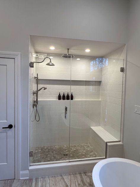 The shower in this new home has a shower seat and a long niche. The tiles are white and the brown floor tiles complement the tranquil setting for the spa-like primary bathroom. White Tile Shower With Bench, Long Shower With Bench, Shower Next To Closet, Showers With Benches Seat, Bench In Shower Ideas, Walk In Shower With Bench Seat, Tub With Bench, Small Shower With Bench, Shower Bench Ideas Built Ins