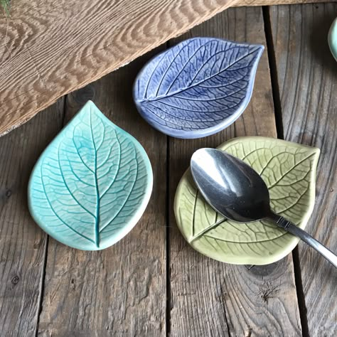 "Set of 3 leaf ring dishes, spoon rests, rustic leaf bowls, leaf ring bowls - Each handmade Earthenware ceramic bowl is impressed with an actual leaves. Perfect for a farmhouse kitchen.   Bowls were slump molded on smooth beach stones to give them shape.   Perfect for holding tea bags, spoons, rings or pills.  One of each color is included in the set of 3: Select Sage/navy blue/ turquoise OR Sage/green/turquoise sets of leaves.  Hand painted with underglaze and gloss glaze and kiln fired to prod Clay Spoon Rest Pottery, Pottery Spoon Rest Ideas, Spoon Rest Pottery Painting Ideas, Hydrangea Leaf, Ring Bowls, Itsekovettuva Savi, Pottery Spoon Rest, Earthenware Ceramics, Beginner Pottery