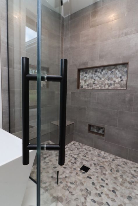 Gray tile shower with light pebble flooring. Glass shower door with black accents. Shower Grey Tile Ideas, Shower Tile Remodel Ideas, Bathroom Shower Tiles Gray, Gray Tile Master Bath, Gray Tiled Bathrooms Ideas, Grey Tile Shower Ideas Master Bath, Large Gray Tile Shower Ideas, Bathrooms With Gray Tile, Black And Grey Shower Tile