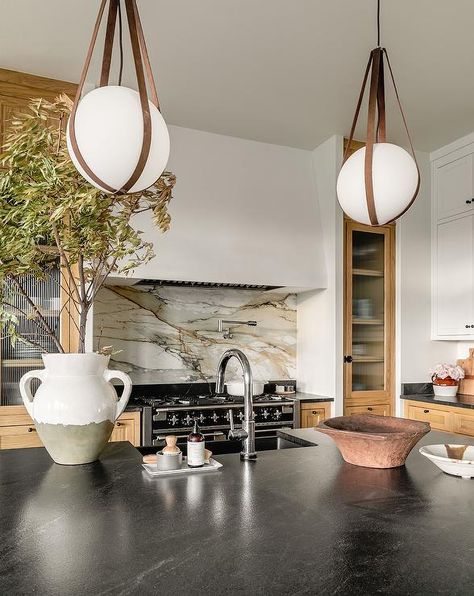 Kitchen features leather strap globe pendants over a black leathered top island with sink that boasts a nickel gooseneck faucet. Neutral Kitchen, Island Countertops, Marble Backsplash, Big Kitchen, Kitchen Backsplash, A Kitchen, Kitchen Inspirations, Round Mirror Bathroom, Interior Designer