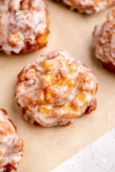 Glazed apple fritters on parchment paper. Dessert Fritters, Fuji Apple Recipes, Fried Apple Fritters, Bake Apples, Easy Apple Fritters Recipe, Homemade Apple Fritters, Live Well Bake Often, Baked Apple Fritters, Fried Apple