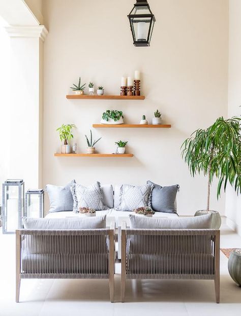 Wrought iron candle lanterns sit beside a white outdoor sofa accented with gray pillows and positioned beneath wooden staggered floating shelves facing side-by-side gray rope accent chairs. Wooden Shelf Design, Home Drawing, Drawing Home, Floating Shelves Living Room, Wooden Floating Shelves, Home Painting, Room Shelves, Estantes Flotantes, Shelf Design