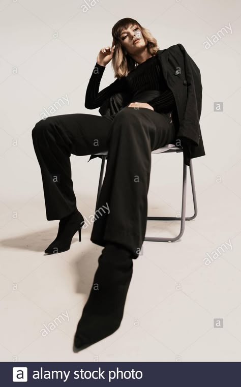 Download this stock image: Portrait beautiful woman with attitude sitting on a chair wearing black clothes posing on white background looking at the camera - 2BGECA9 from Alamy's library of millions of high resolution stock photos, illustrations and vectors. Sitting Down On Chair Poses, Pose Reference Photo Sitting Chair, Woman Sitting On A Chair Pose Reference, Power Sitting Pose, Person Sitting In Chair Pose, Poses On The Chair, High Fashion Chair Poses, Powerful Sitting Pose, Woman Sitting In Chair Pose