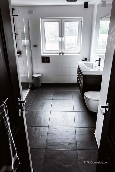 This bathroom is all about keeping things sleek and simple. The crisp white walls are the perfect contrast to the dark flooring. Bathroom Black Floor White Walls, Small Bathroom Dark Floor, Bathrooms With Black Floors, Dark Tile Bathroom Floor, Bathroom Dark Floor, Bathroom Black Floor, Dark Bathroom Floor Tile, Dark Floor Bathroom, Dark Tile Bathroom