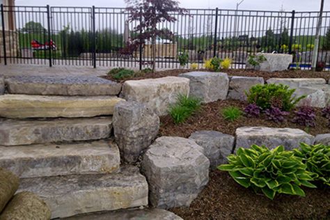 Austin Stone Retaining Wall, Armour Stone Landscaping Front Yard, Landscape Ideas Retaining Wall, Armour Stone Retaining Wall, Tiered Garden Ideas, Landscape Retaining Wall, Sloped Landscape, Lakehouse Exterior, Boulder Retaining Wall