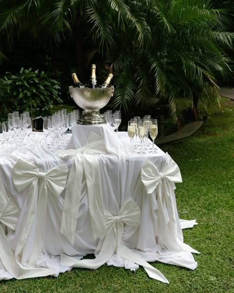 Looking for sophisticated wedding decor ideas? This exquisite champagne table setup, adorned with luxurious white bows and flowing drapery, is perfect for a garden wedding or outdoor celebration. The silver champagne bucket adds a touch of timeless elegance. Ideal for event planners and brides looking for unique champagne station inspirations. Champagne Table Setting, Wedding Table Cloth Ideas, Winter Wedding Trends, Enchanted Wedding Theme, Champagne Table, Wedding Drapery, Bride Groom Table, Honey Wedding, White Chapel