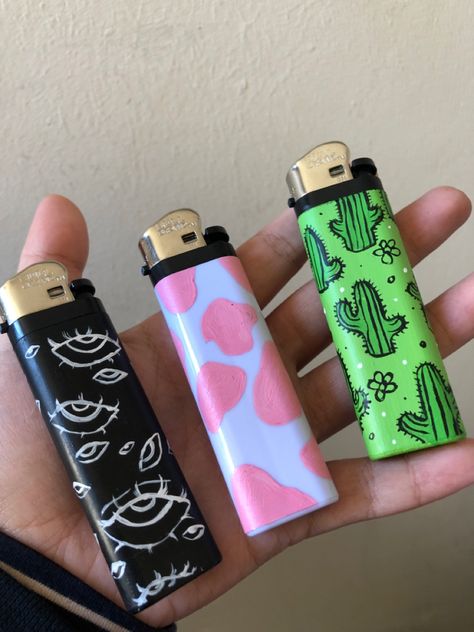 Acrylic paint designs: creepy eyes, pink cow print, cute green cacti Aesthetic Lighter Drawing, Drawing On Lighter Ideas, Painting Lighters Diy, Lighter Ideas Diy, Lighter Art Diy, Painting On Lighter, Painted Lighters Aesthetic, Diy Lighter Painting, Cool Lighter Aesthetic