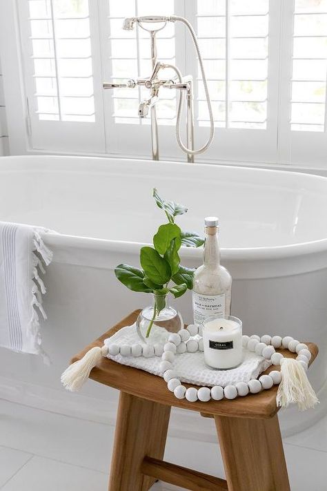 Bathroom features a teak sawhorse bathtub stool with white decorative beads and a vintage oval bathtub with a polished nickel tub filler. Bathtub Side Table Ideas, Bathroom Stools Decor Ideas, Bathroom Stool Ideas, Bathroom Stools Decor, Soaking Tub Decor, Bathtub Side Table, Bathtub Stool, Bathroom Stools, Bathtub Light