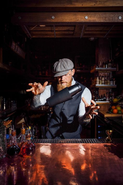 Bartender with beard and vintage hat flipping cocktail shaker mid air at the bar with bottles and wooden shelves around him Bartenders Photography, Sarah King, Boston Style, Most Popular Cocktails, Bartender Tools, Tiki Mugs, Popular Cocktails, Boston Fashion, Restaurant Photography