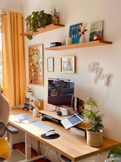 Cozy home office setup featuring a wooden desk under sunlight from a window with yellow curtains. The space is decorated with green plants on floating shelves, motivational posters, and a neon sign saying 'let's play' above the desk. A laptop and monitor provide a functional work area. Cozy Desk Setup, Interior Design Layout, Cozy Desk, Desk Inspiration, Aesthetic Space, Gaming Room Setup, Home Office Setup, Home Office Space, Room Setup