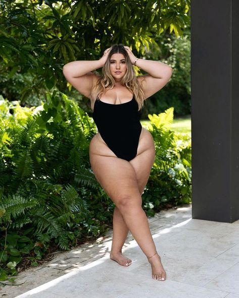 A woman poses outdoors in a black one-piece swimsuit, standing barefoot on a stone patio. She places her hands on her head, surrounded by lush greenery in the background Cheeky Quotes, Dark Beauty Photography, Top Summer Outfits, Positivity Quotes, Seductive Clothes, Curvy Women Outfits, Curvy Model, Plus Size Swimsuits, Curvy Girl Outfits