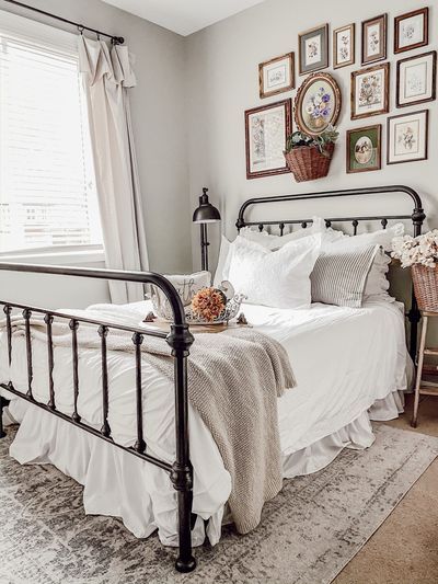 A super small cottage style guest bedroom with Benjamin Moore Vale Mist (light sage green) walls, a black iron farmhouse metal bedframe, white ruffle bedding and cream throws. A vintage boutique rugs greay and cream rug, and a chippy old wooden ladder with a basket of faux flowers. Vintage gold framed floral accent wall. – Rain and Pine #farmhouse #farmhousedecor #cottage #cottagedecor #neutraldecor #vintagedecor #guestbedroom #farmhousebedroom #cottagebedroom Black Metal Bed Frame White Bedding, Black Metal Bed Frame Styling, Black Farmhouse Bed Frame, Bed Frame Iron, Vintage Bed Frame Metal, Black Metal Bedframe Bedroom, Black Metal Bed Frame Bedroom Decor, White Iron Bed Frame Bedroom, Black Iron Bed Decor