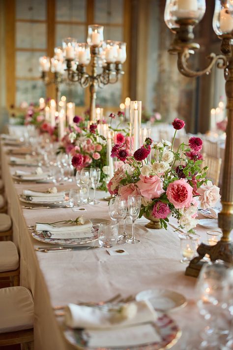 Here, we notice golden candelabras, candles, colorful flowers with deep pink, burgundy, and creamy white hues, and colorful charger plates to complete the look. Wedding Planner: @primaveradreams Wedding Reception Flower Centerpieces, Candelabra With Flowers Centerpiece, Pink Italian Wedding, Red And Pink Wedding Florals, Strawberry Wedding Theme, Simple Wedding Centerpieces Long Tables, Berry Wedding Colors, Long Table Wedding Centerpieces, Pink Wedding Aesthetic