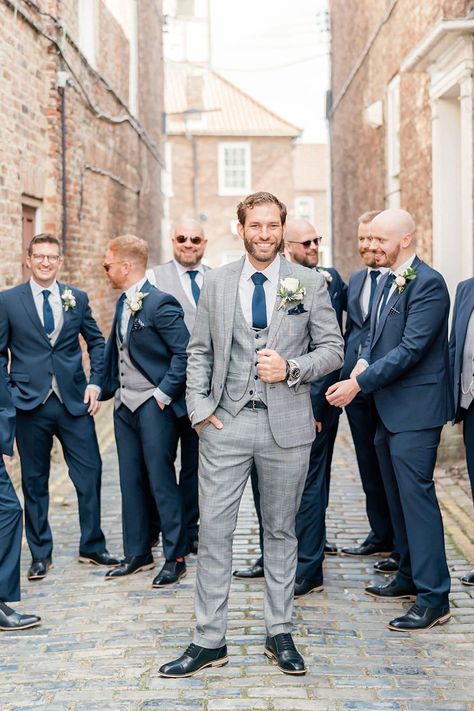 Groom in a light grey check wedding suit with his groomsmen in navy three-piece suits standing behind him | Caro Patrick Photography Grey Suit Navy Tie Wedding, Grey Suits For Men Color Combos, Grey Groom Suit With Bride, Grey Suit With Navy Tie, Grey And Blue Suit, Grey Suit Blue Tie, Navy Grey Suit, Groomsmen Attire Grey, Grey Tuxedo Wedding