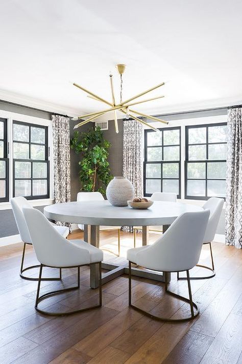 White and gold dining chairs surround a round concrete and wood dining table illuminated by a brass wand chandelier. White Round Dining Table, Gold Dining Chairs, Circular Dining Table, Transitional Dining Room, Gold Dining, Grey Dining Room, Concrete Dining Table, Round Dining Room, Dining Room Inspiration