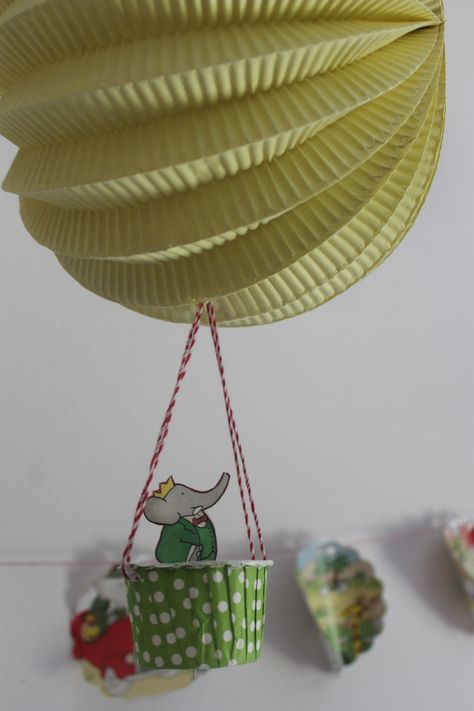 I purchased a damaged book from Amazon and cut it up for decorations. Shown here in the garland as well as a hot air balloon passenger. (made with a paper lantern, twine, and a cupcake liner) Babar Party Babar Themed Party, Babar Birthday Party, Book Themed Birthday Party, 21 Balloons, Elephant Birthday Party, Children's Book Week, Travel Baby Shower Theme, Elephant Party, School Doors