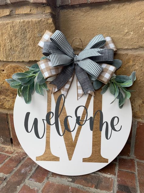 "What a great way to welcome friends and visitors to your home! This initial welcome door hanger is painted white and featured a stained initial with charcoal grey lettering. Lambs ear and a multi-layered bow adorn the top.  If you would like the door hanger done in a different color combo, simply message us.  Please allow 1-2 weeks processing time for your order. Send a message if you would like to customize colors.  Base round is made of 1/2\" baltic birch plywood with rounded edges.  Back of Initial Door Hanger, Personalized Wreaths, Welcome Signs Front Door, Welcome Door Hanger, Door Hangers Diy, Welcome Door Signs, Wooden Signs Diy, Door Signs Diy, Wooden Door Signs