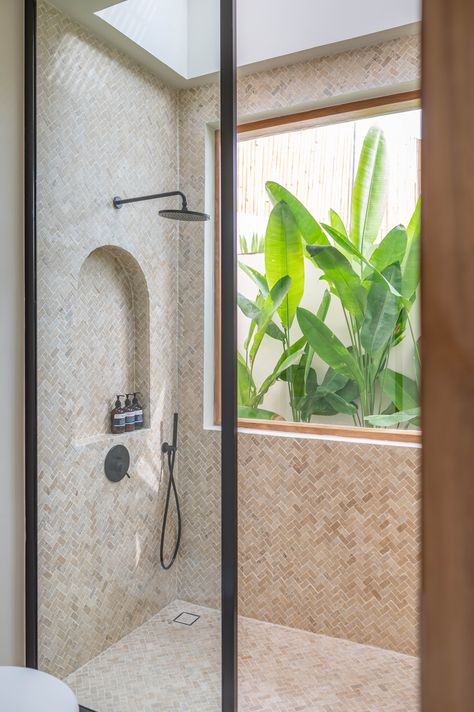 A walk-in shower in a Bali villa with beige textured tiles, a black showerhead, and a large window offering a lush garden view, creating a tropical spa-like atmosphere. Bali Villa Bathroom, Bali Bathroom, Villa Bathroom, Tropical Showers, Neutral Tile, Bali Villa, Bathroom Features, Spa Like Bathroom, Tropical Twist