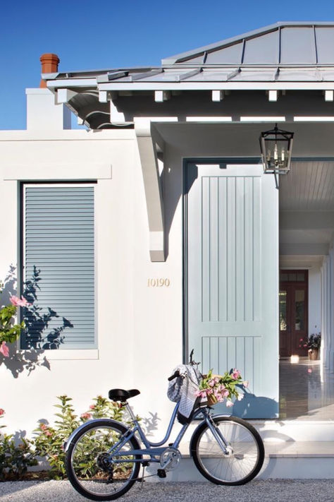 Outside her modern coastal home, designer @leahmullerinteriors_ created a sophisticated tropical aesthetic using light blue paneled doors and Bahama shutters that pop against the bright white concrete exterior. Above the front porch, our beloved Darlana Small Hanging Lantern by Chapman & Myers enhances the Florida abode's curb appeal with a classic bronze form featuring geometric details and clear glass. 📷: @jessglynnphoto Charleston Gas Lanterns, Front Porch Lanterns, Outdoor Wall Lantern Brass, Visual Comfort Holborn Lantern, Visual Comfort Outdoor Lighting, Porch Lantern, Bahama Shutters, Concrete Exterior, Antique Brass Lantern Pendant