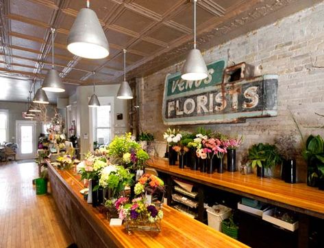 I know it sounds crazy but I want a reclaimed brick wall like this and old wood, highly lacquered counters for work tables in the garage plus the two midcentury tables from Uncle Eugene's garage.... plenty of space for work and play....    @ Love the Blooms Reclaimed Brick Wall, Flower Shop Display, Flower Shop Interiors, Florist Studio, Flower Shop Design, Reclaimed Brick, Flower Boutique, Flower Store, Florist Shop