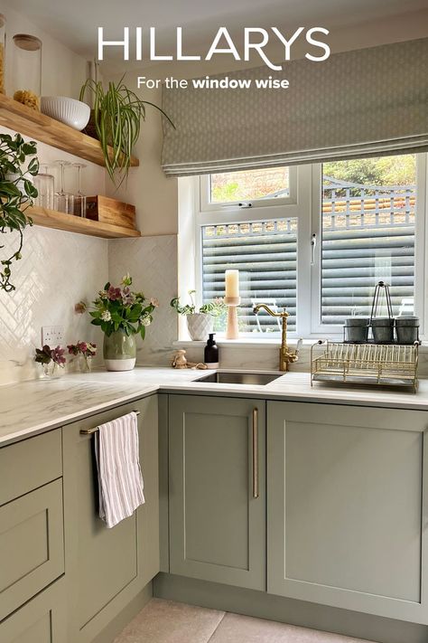 A cream-beige Roman blind in a farmhouse style kitchen with sage green units and marble worktops. There are lots of fresh flowers and plants on the shelves around the kitchen. Green Kitchen Blinds, Roman Blinds Kitchen, Farmhouse Style Kitchen Decor, Sage Kitchen, Sage Green Kitchen, Cream Kitchen, Beige Kitchen, Kitchen Blinds, Home Entrance Decor