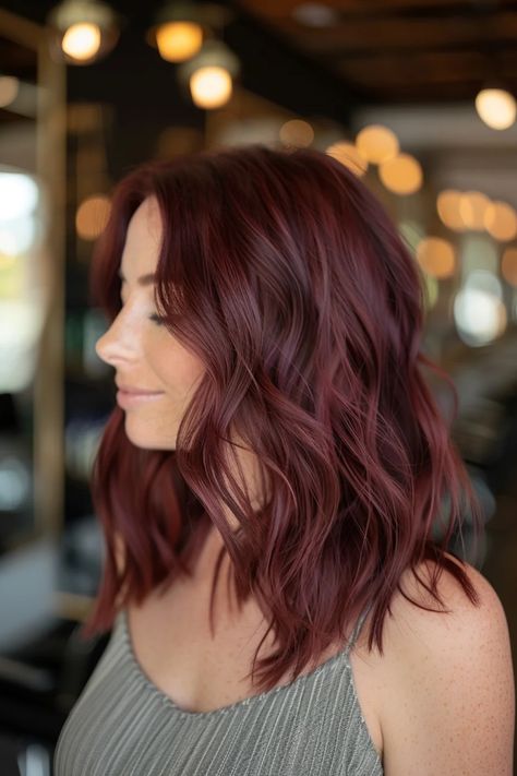 Woman with wavy, auburn hair smiling in a salon setting. Medium Length Haircut Burgundy, Rose Brunette Balayage, Brown To Red Color Melt, Brown Hair Maroon Highlights, Burgundy Medium Length Hair, Burgundy Hair Blue Eyes Pale Skin, Chocolate Red Hair Color Burgundy, Brown To Burgundy Hair, Maroon Hair Highlights