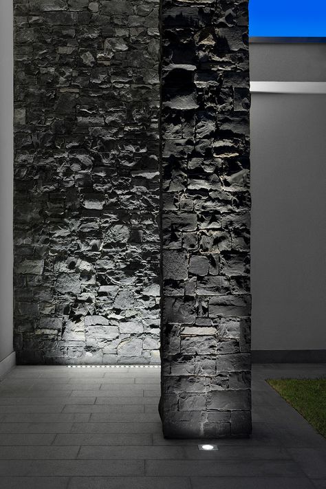 The exterior of the house is characterised by light-coloured surfaces combined with dark grey stone walls. The chosen lighting highlights the stone surface with a wall-grazing effect that underlines the surfaces’ materiality. Wall Grazing Lighting, Grey Stone Exterior, Stone Wall Lighting, Boundary Wall Designs, Stone Wall Light, Modern Exterior Lighting, Exterior Lighting Design, Grey Stone Wall, Outdoor Decor Ideas