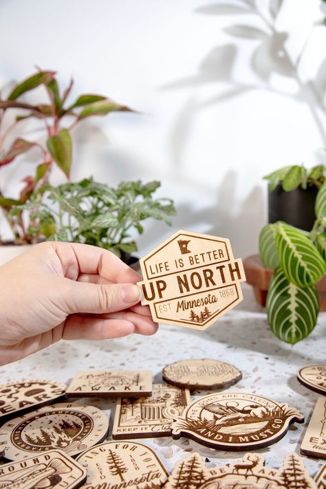 Life is Better Up North Engraved Wood Magnet Our Wood Magnets are designed and crafted in-house from quality 1/4 in. engraved plywood. Magnets make great souvenirs from favorite travels, keep track of notes and those pesky to-do lists, or add a little humor to your home or office. +Magnet is about 3 in by 3 in in size +Quality 1 in. Black Ceramic button Magnet and Attached with a 2-Part Epoxy for strength. +Wood is given a matte finish to seal laser engraving. Please note the color can vary from Laser Engraving Ideas Projects, Laser Cut Wood Jewelry, Wood Engraved Gifts, Laser Cut Coaster, Wood Magnets, Laser Crafts, Laser Vision, Canvas Banners, Diy Laser Cut