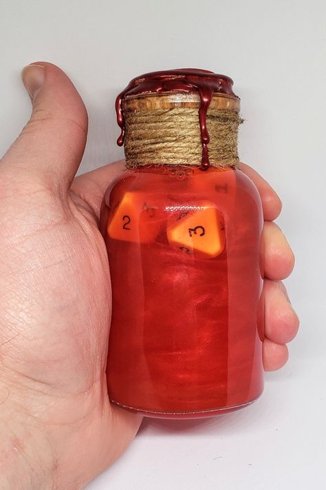 A large glass vial is held in hand. The glass is sealed with cork, twine, and red wax. Inside the glass bottle is a a swirling red liquid and several gaming dice. Dnd Dice Roller, Dnd Health Potion, Dnd Potions, Potion Of Healing, Potion Maker, Sensory Jars, Lab Decorations, Health Potion, Dnd Party