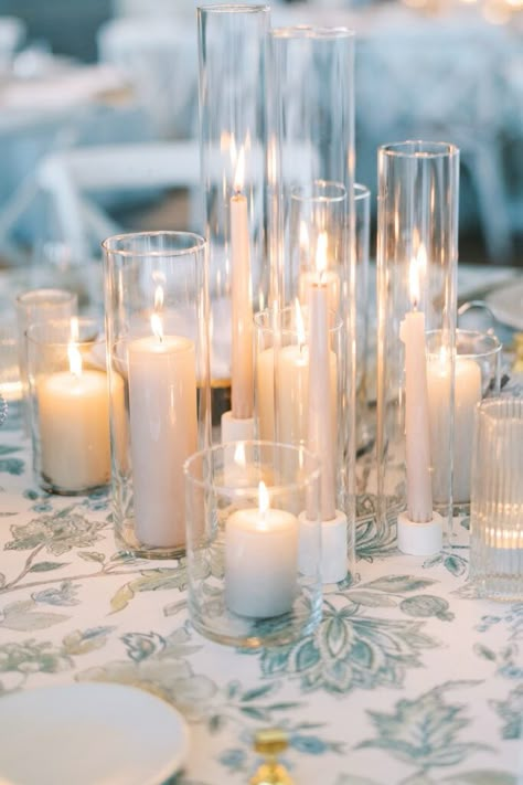 Colored pillar and taper candle centerpiece with blue print linen. Neon Light Sweetheart Table, Candle Trio Centerpiece, Nonfloral Centerpiece Ideas, Candle Holders Decor Ideas, Taper Candle Centerpiece, Candlestick Centerpiece Wedding, Round Table Centerpieces, Little Wedding Details, Taper Candles Wedding